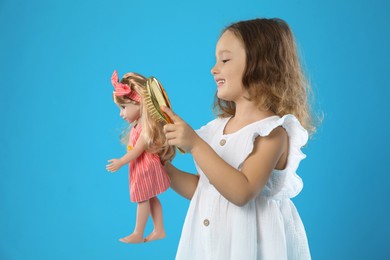 Photo of Cute little girl brushing doll's hair on light blue background