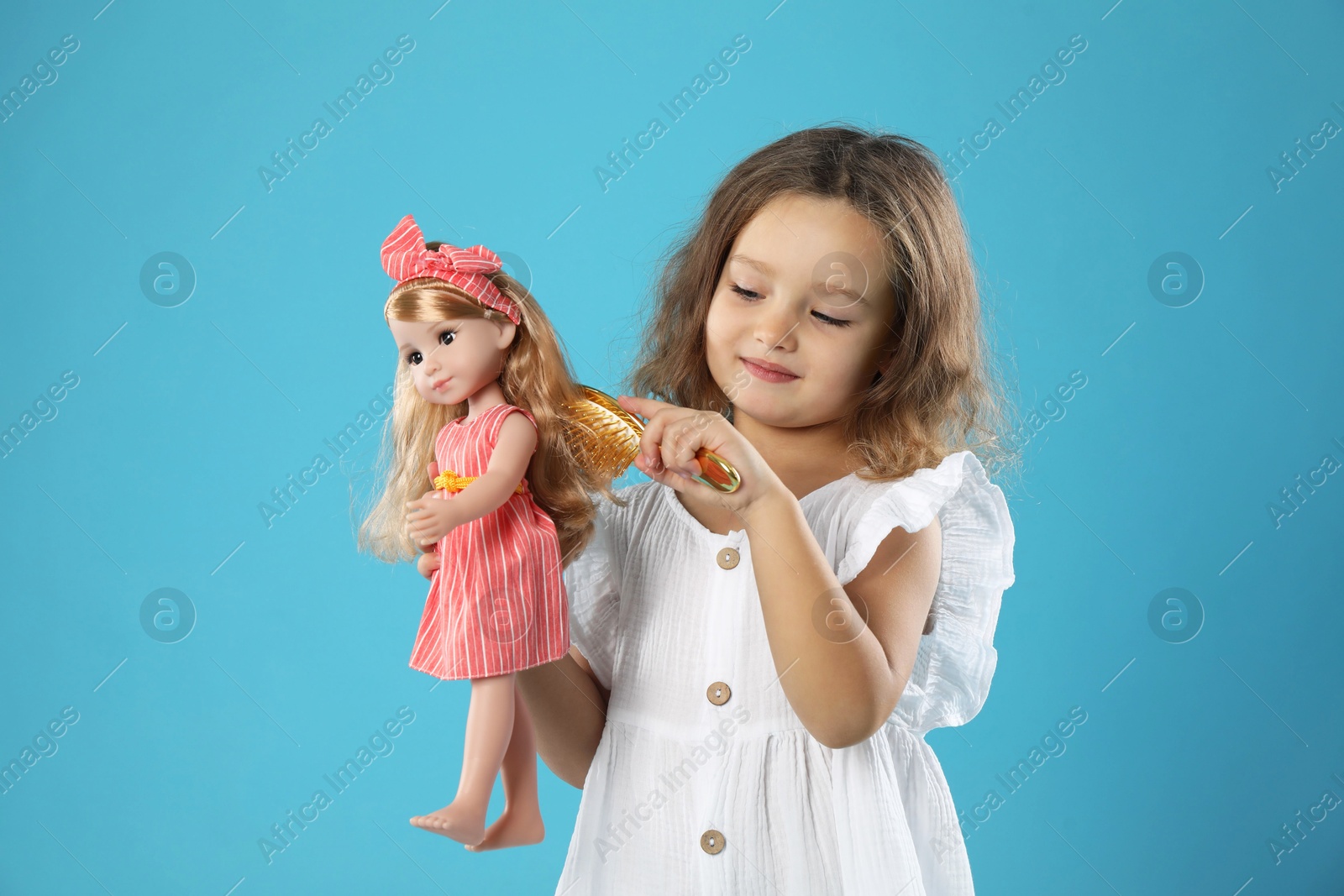 Photo of Cute little girl brushing doll's hair on light blue background