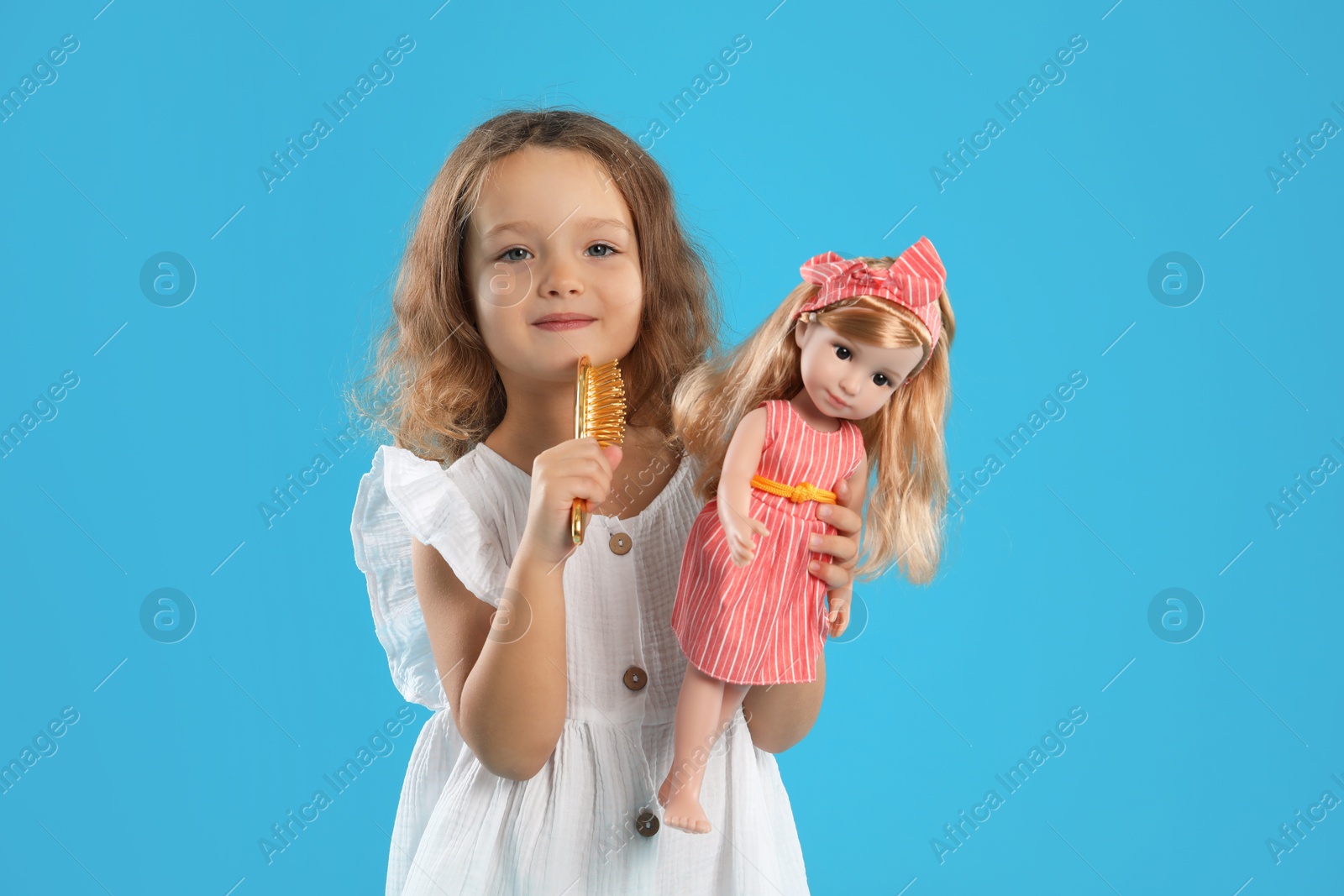 Photo of Cute little girl brushing doll's hair on light blue background