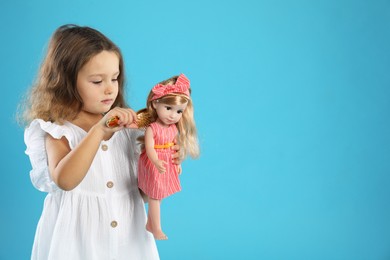 Photo of Cute little girl brushing doll's hair on light blue background. Space for text