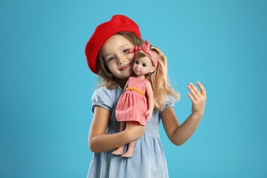 Photo of Cute little girl with doll on light blue background