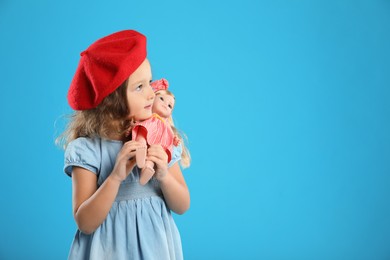 Photo of Cute little girl with doll on light blue background. Space for text