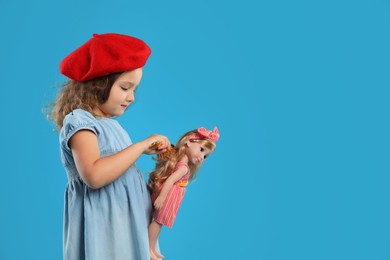 Photo of Cute little girl brushing doll's hair on light blue background. Space for text