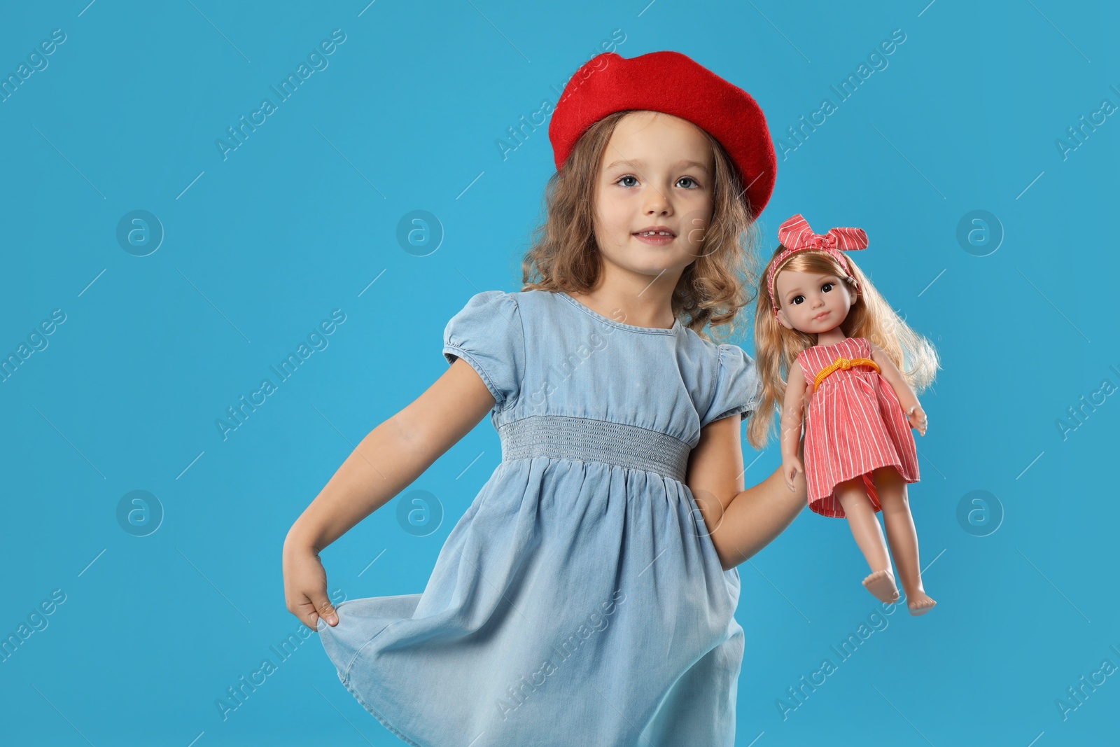 Photo of Cute little girl with doll on light blue background