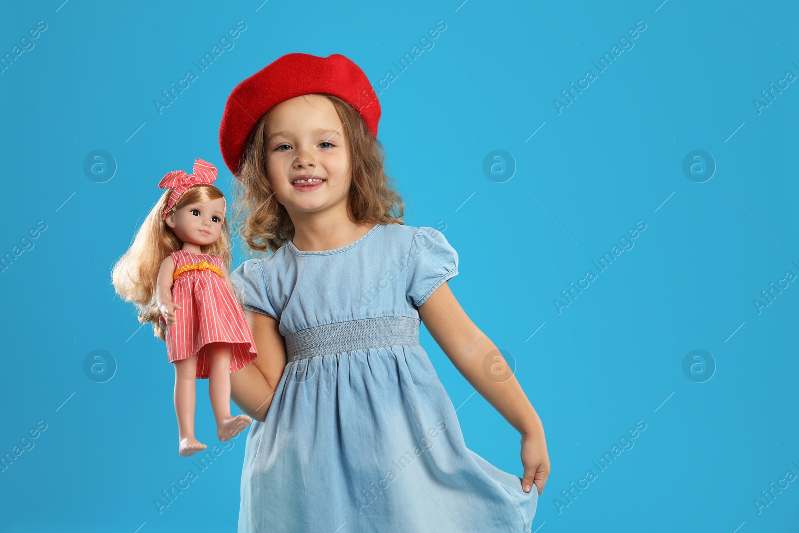 Photo of Cute little girl with doll on light blue background. Space for text