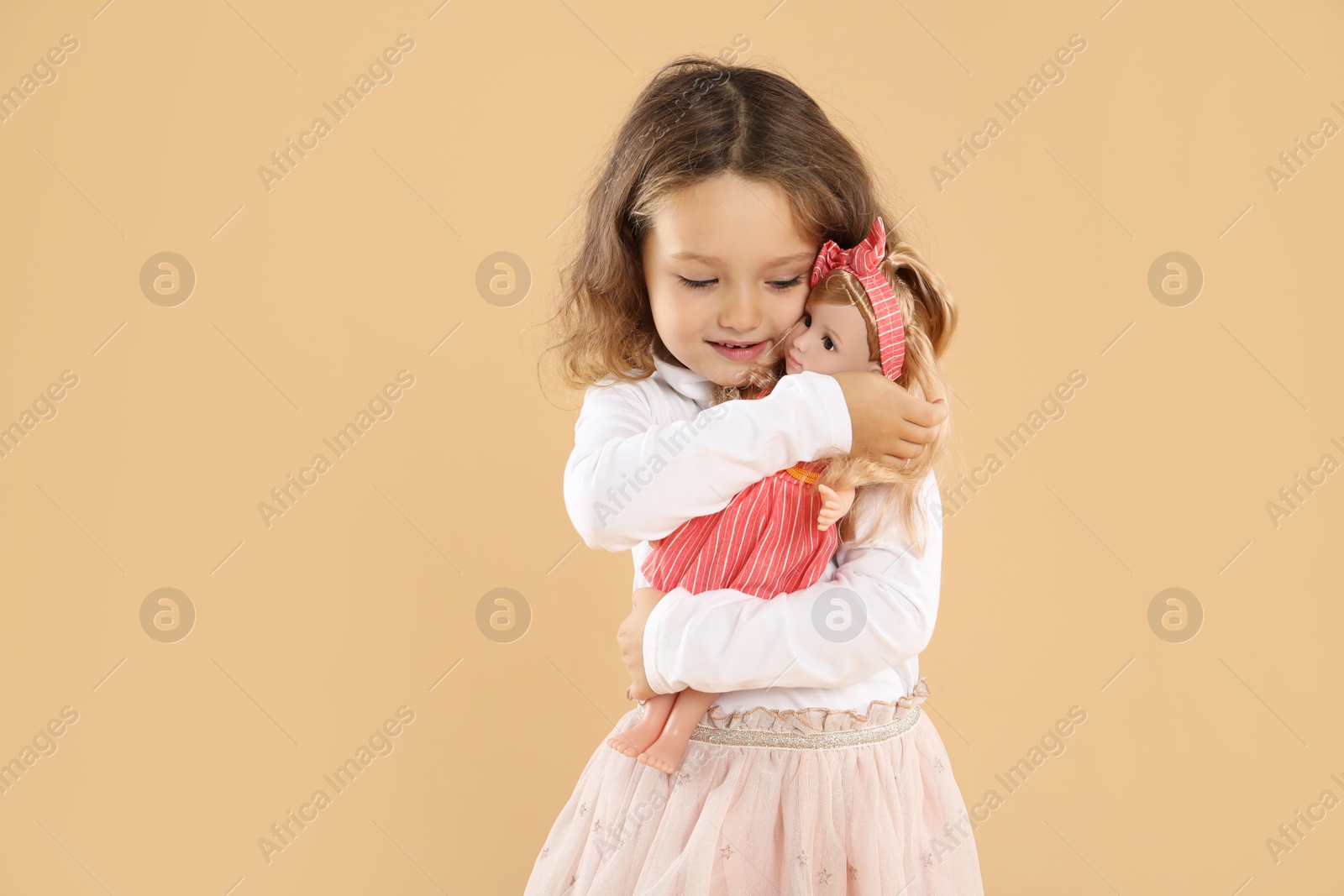 Photo of Cute little girl with doll on beige background. Space for text