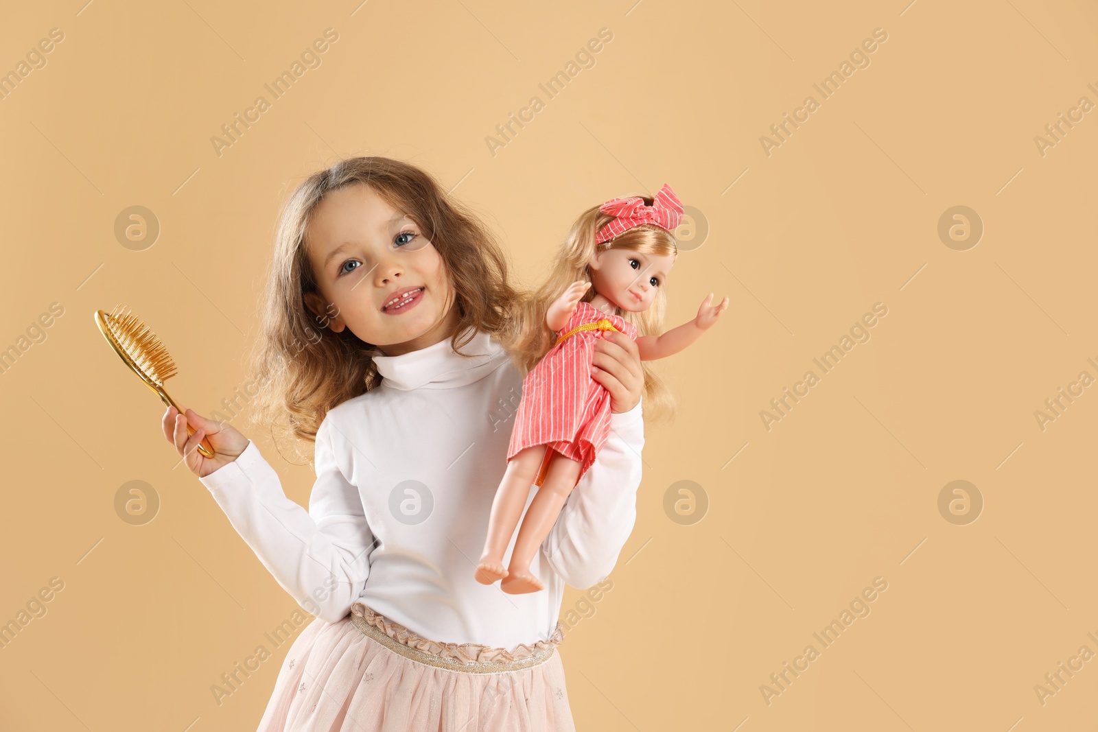 Photo of Cute little girl with doll and brush on beige background. Space for text