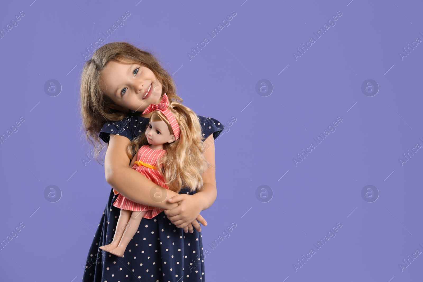 Photo of Cute little girl with doll on purple background. Space for text