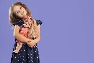 Photo of Cute little girl with doll on purple background. Space for text