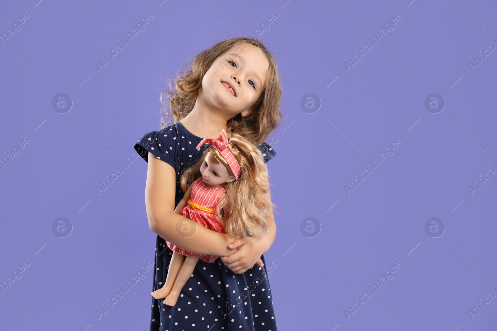 Photo of Cute little girl with doll on purple background. Space for text