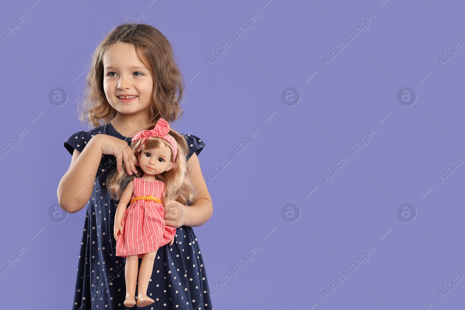 Photo of Cute little girl with doll on purple background. Space for text