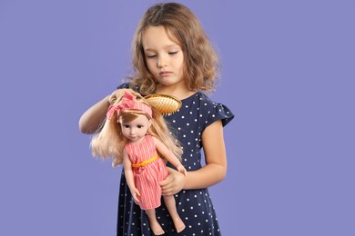 Photo of Cute little girl brushing doll's hair on purple background