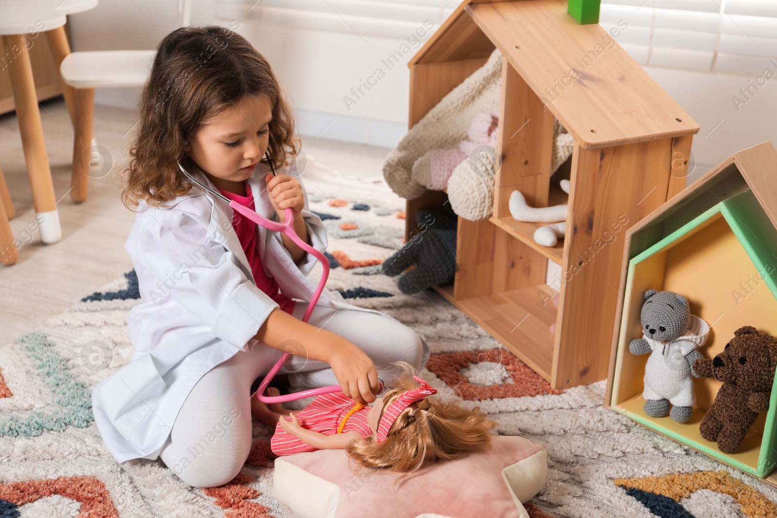 Photo of Cute little girl playing doctor with doll at home