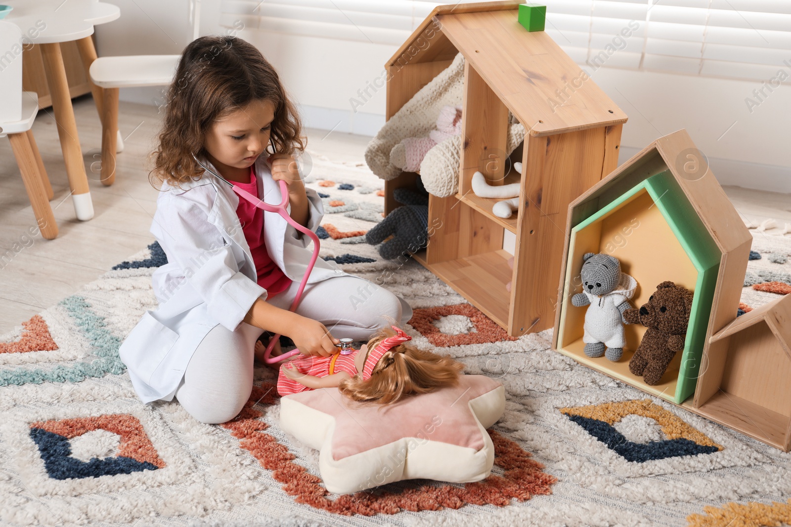 Photo of Cute little girl playing doctor with doll at home