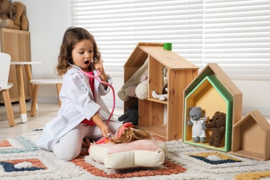 Photo of Cute little girl playing doctor with doll at home