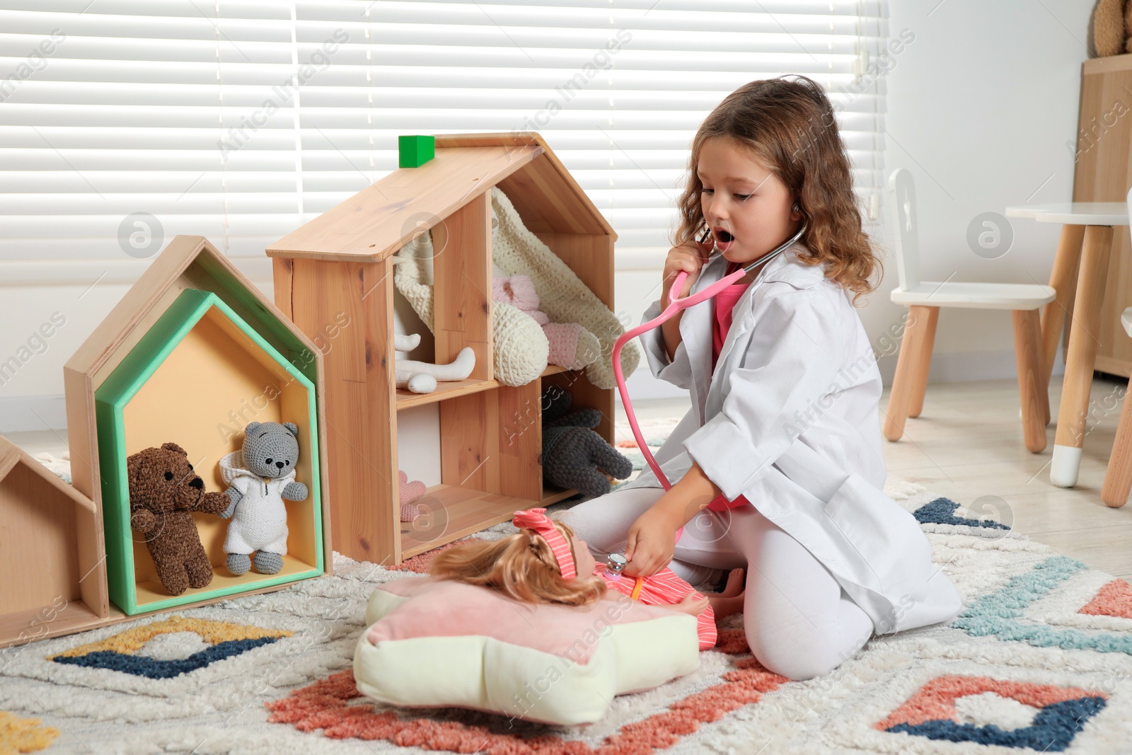 Photo of Cute little girl playing doctor with doll at home