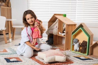 Photo of Cute little girl playing doctor with doll at home