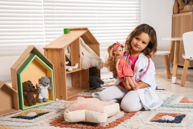 Photo of Cute little girl playing doctor with doll at home