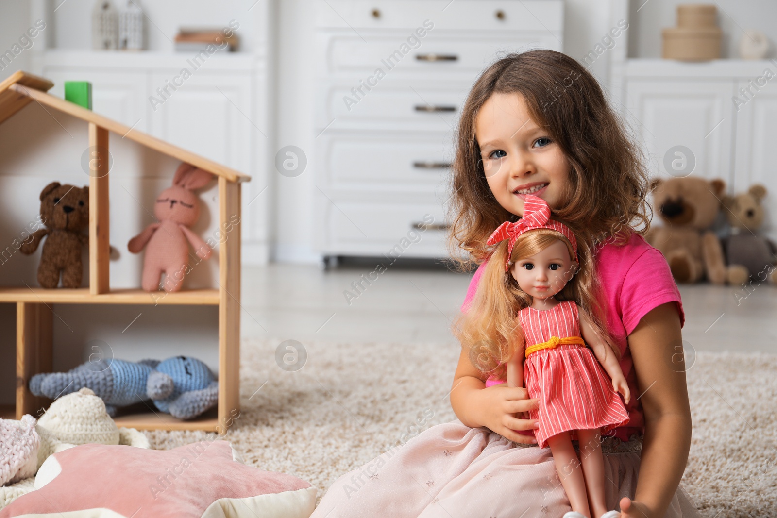 Photo of Cute little girl playing with doll on floor at home