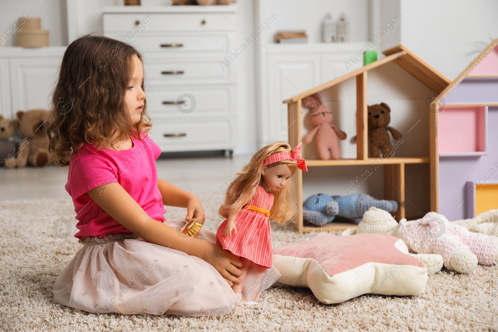 Photo of Cute little girl brushing doll's hair at home