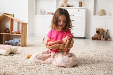 Photo of Cute little girl playing with her doll on floor at home