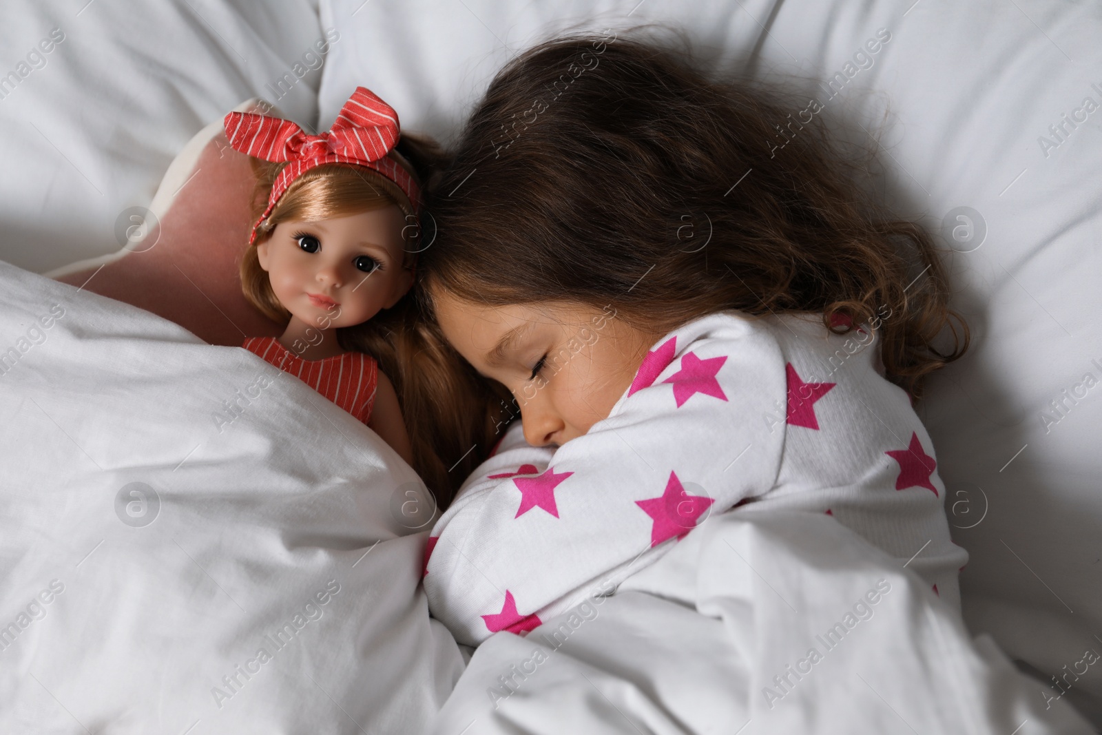 Photo of Little girl sleeping with doll in bed, top view