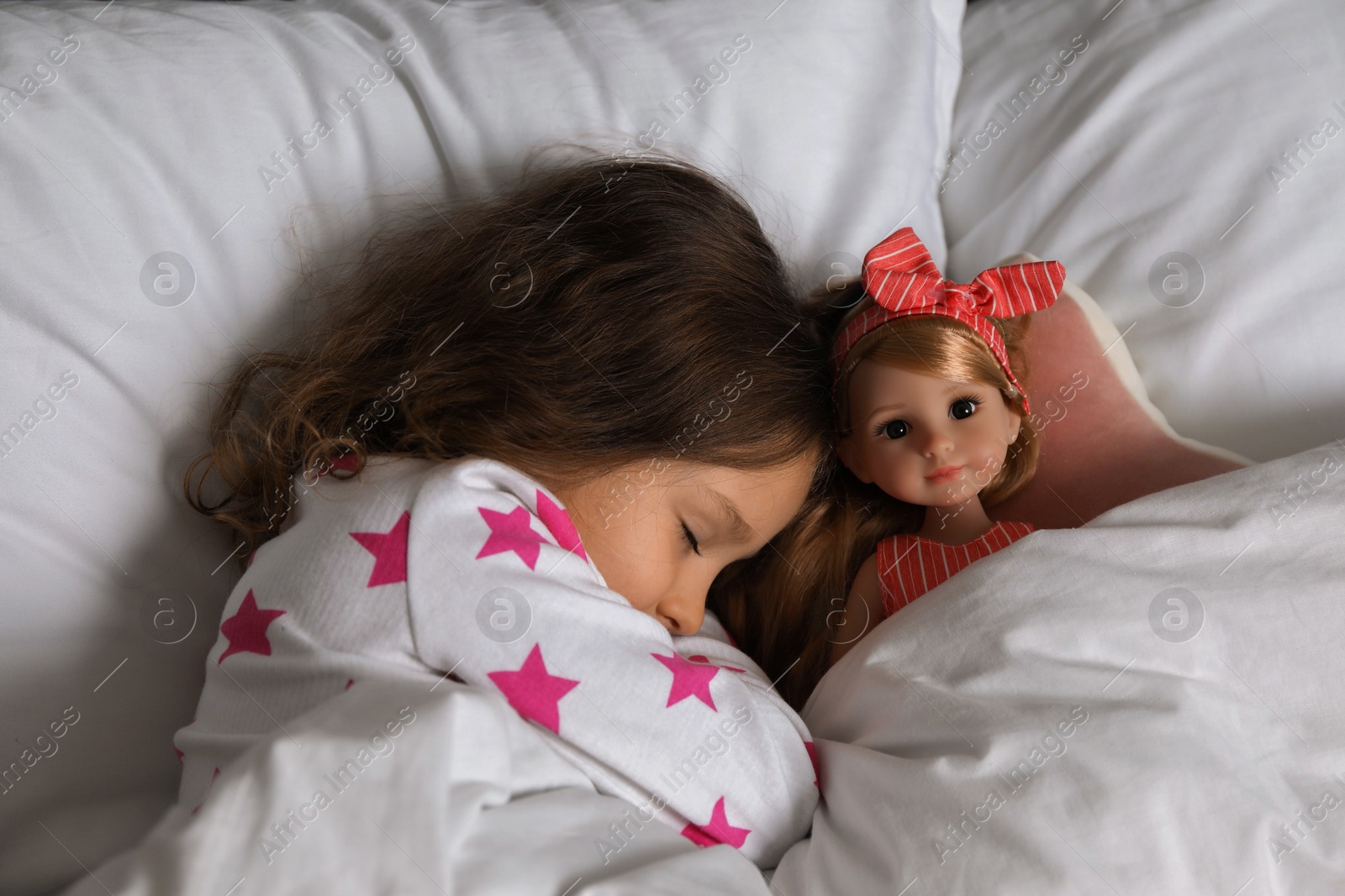 Photo of Little girl sleeping with doll in bed, top view