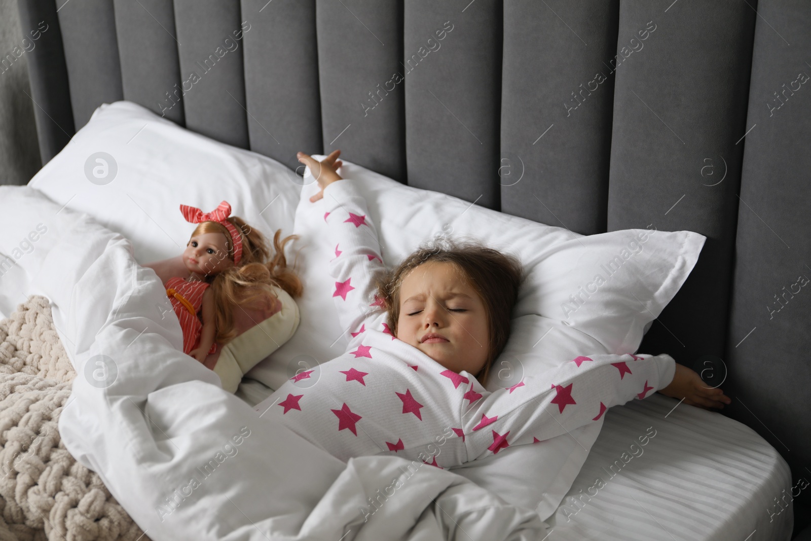 Photo of Cute little girl stretching near her doll in bed