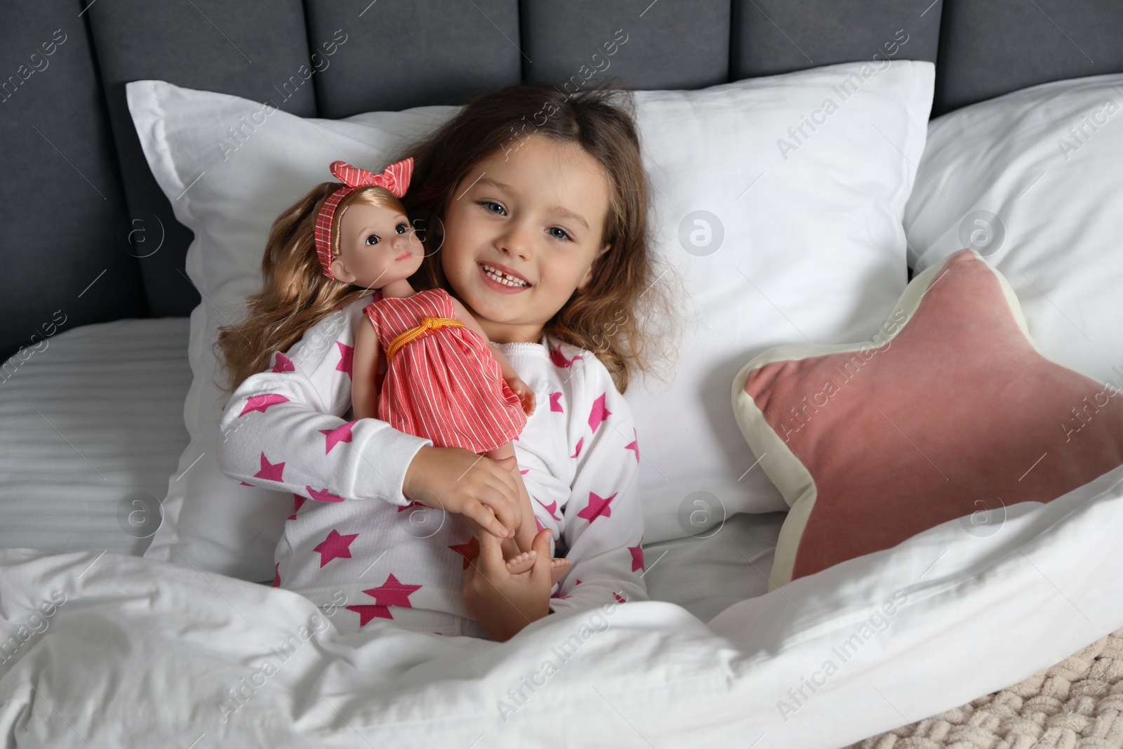 Photo of Cute little girl playing with doll in bed