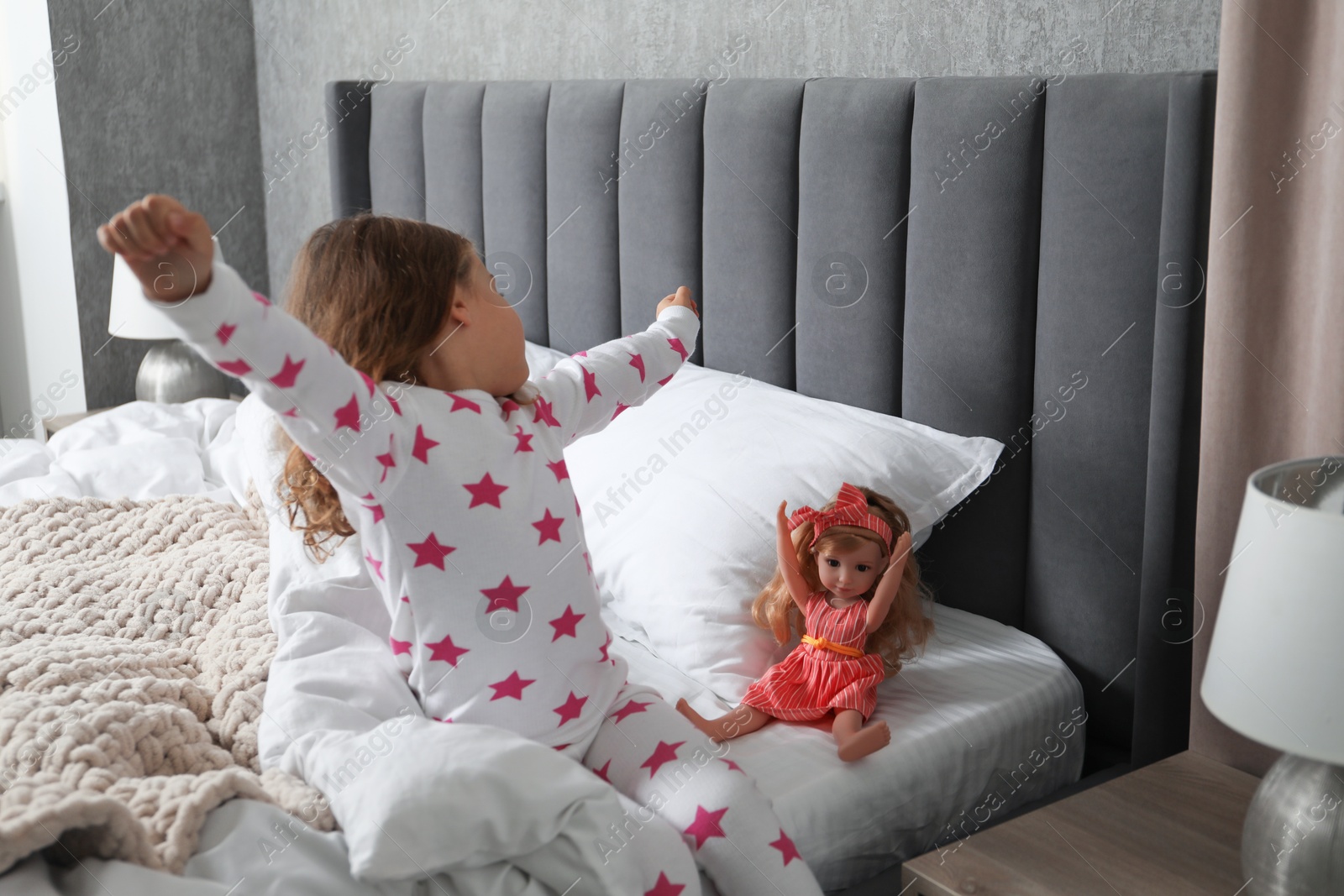 Photo of Little girl stretching while her doll sitting on bed