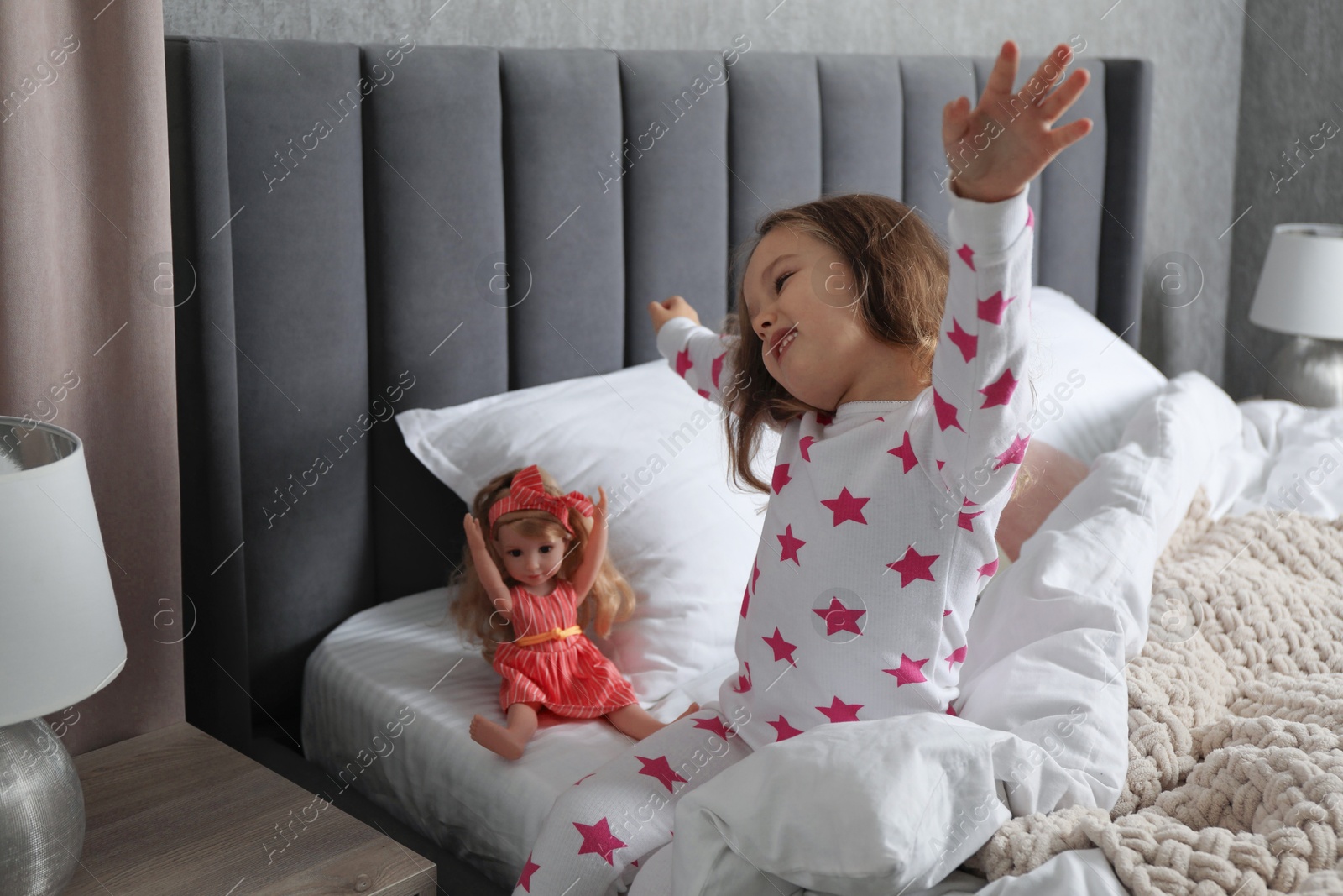 Photo of Cute little girl stretching while her doll sitting on bed