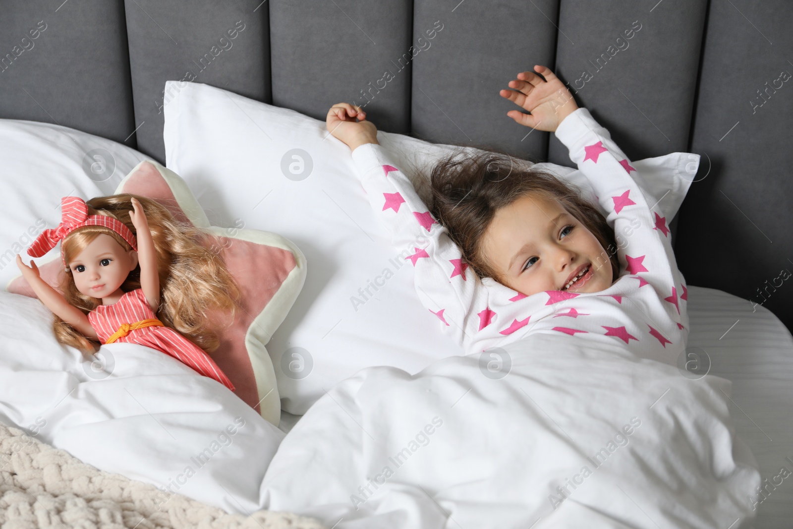 Photo of Cute little girl stretching near her doll in bed