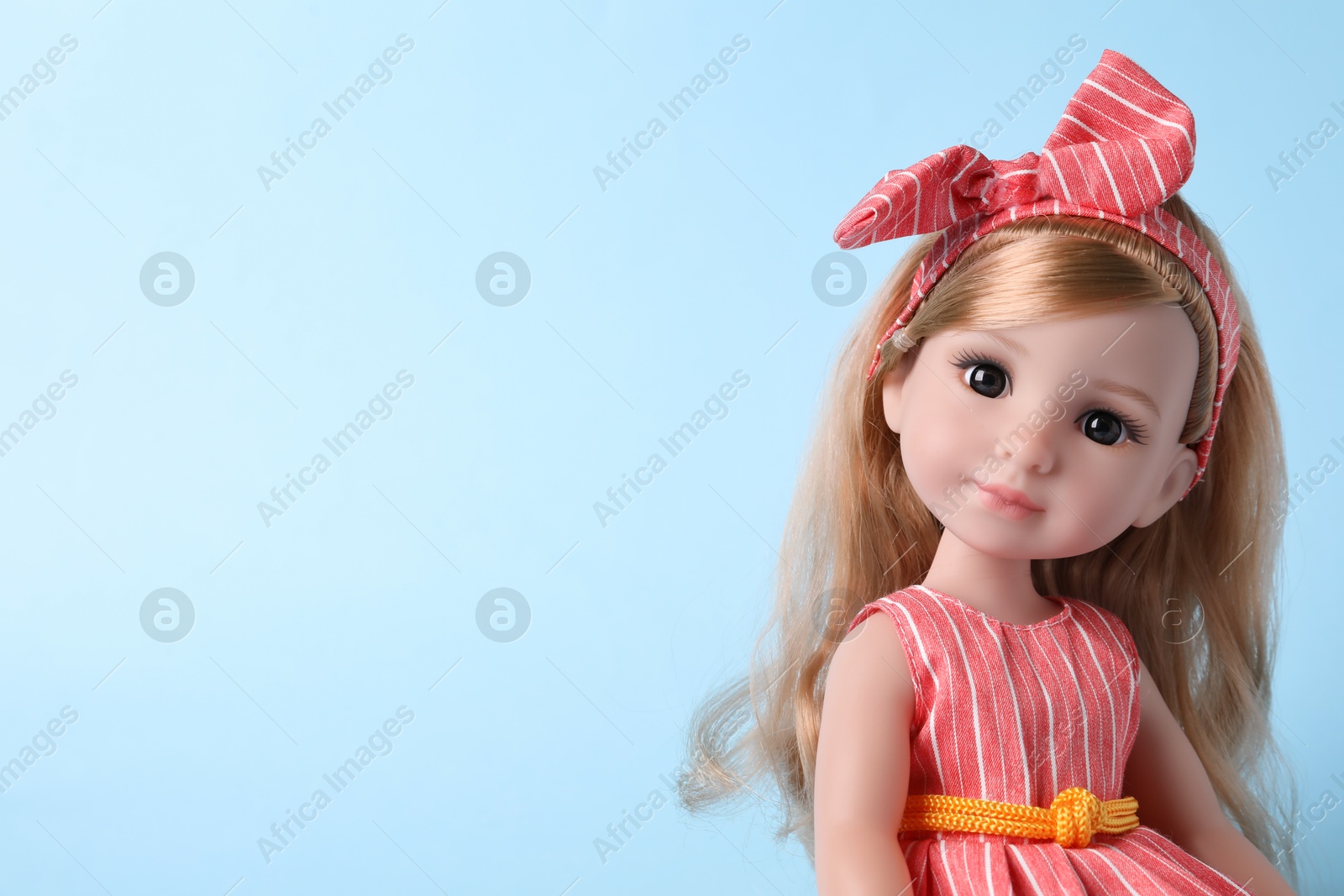 Photo of Beautiful doll in dress and headband on light blue background, closeup. Space for text