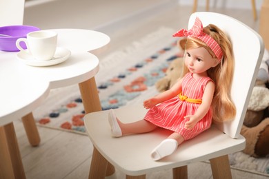 Beautiful doll in dress and headband on white chair indoors