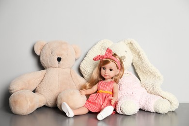 Beautiful doll, teddy bear and toy bunny on grey table near white wall