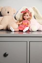 Photo of Beautiful doll, teddy bear and toy bunny on grey chest of drawers near white wall