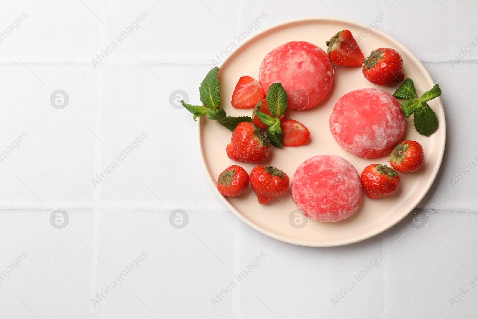 Photo of Delicious mochi, strawberries and mint on white tiled table, top view. Space for text