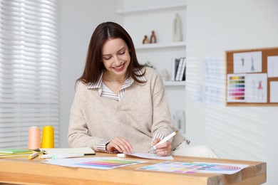 Photo of Fashion designer drawing sketch of clothes at wooden table in workshop