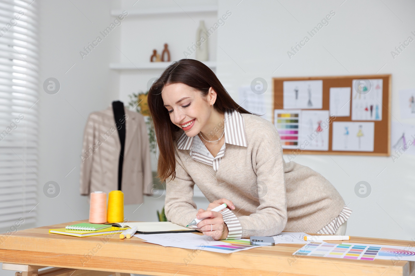 Photo of Fashion designer drawing sketch of stylish clothes at wooden table in workshop