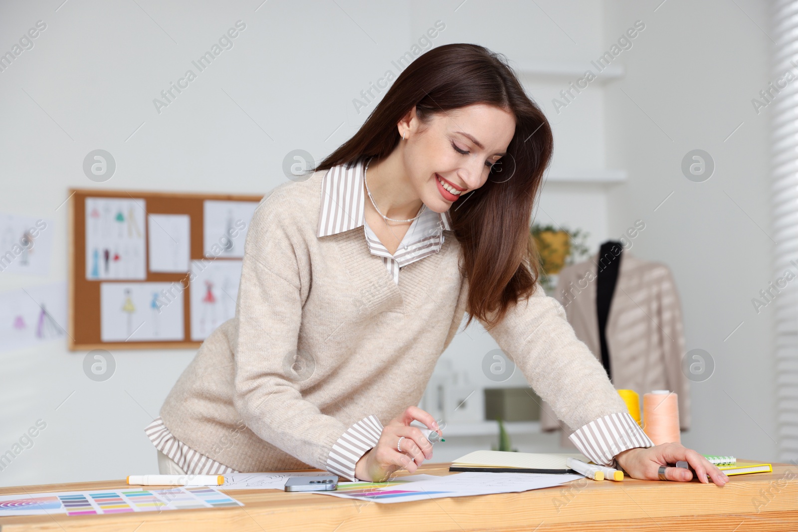 Photo of Fashion designer drawing sketch of stylish clothes at wooden table in workshop