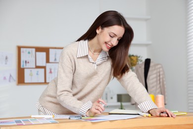 Fashion designer drawing sketch of stylish clothes at wooden table in workshop