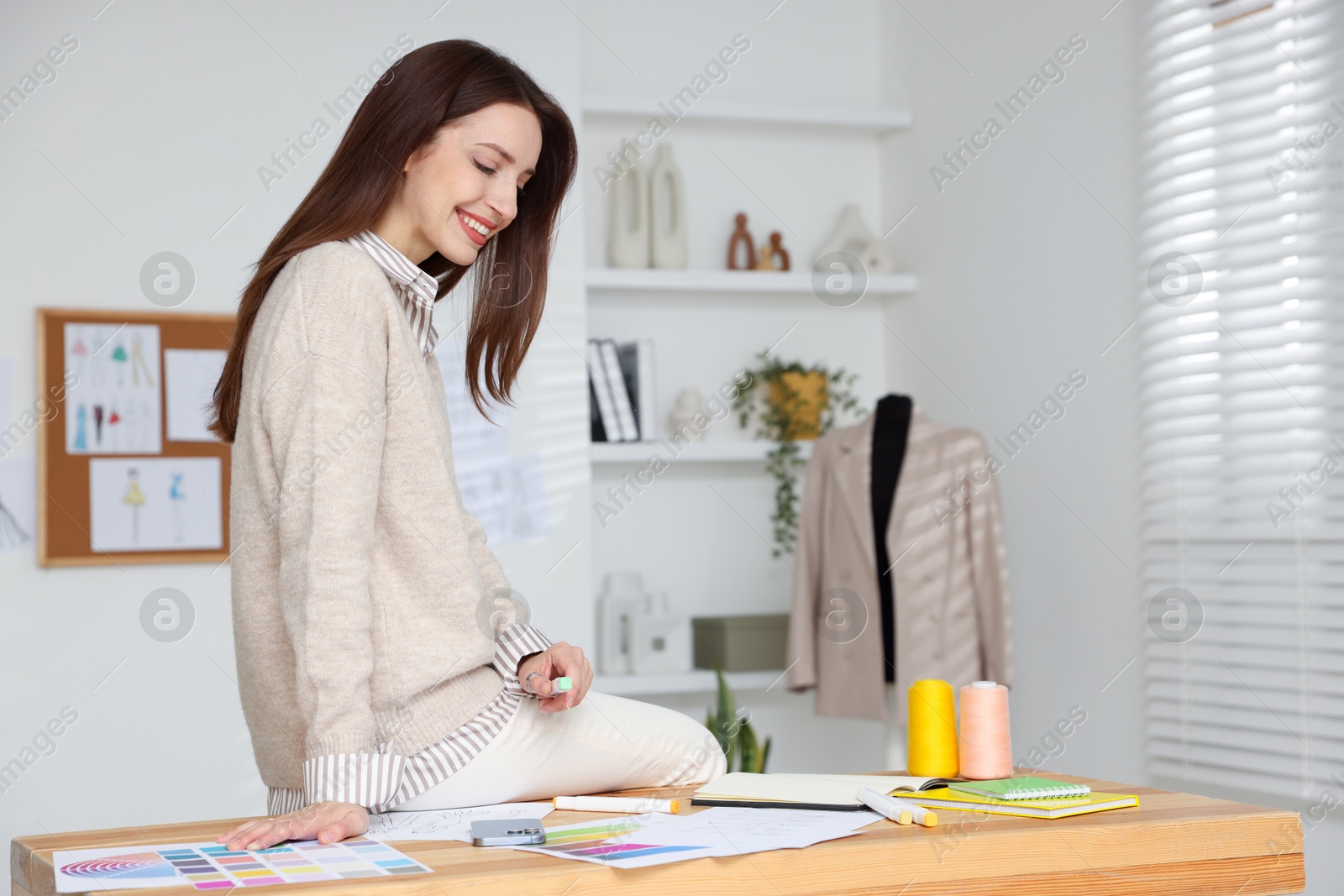 Photo of Fashion designer with marker sitting on wooden table in workshop, space for text