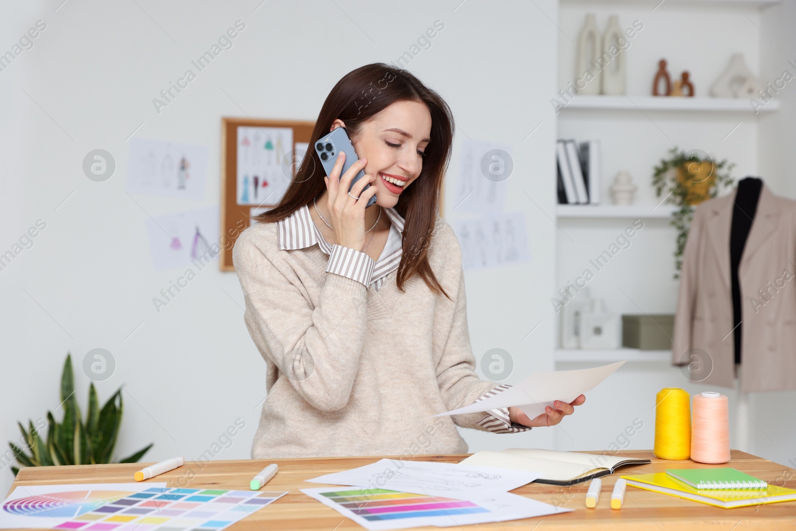 Photo of Fashion designer talking on smartphone at wooden table in workshop