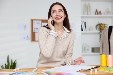 Fashion designer talking on smartphone at wooden table in workshop