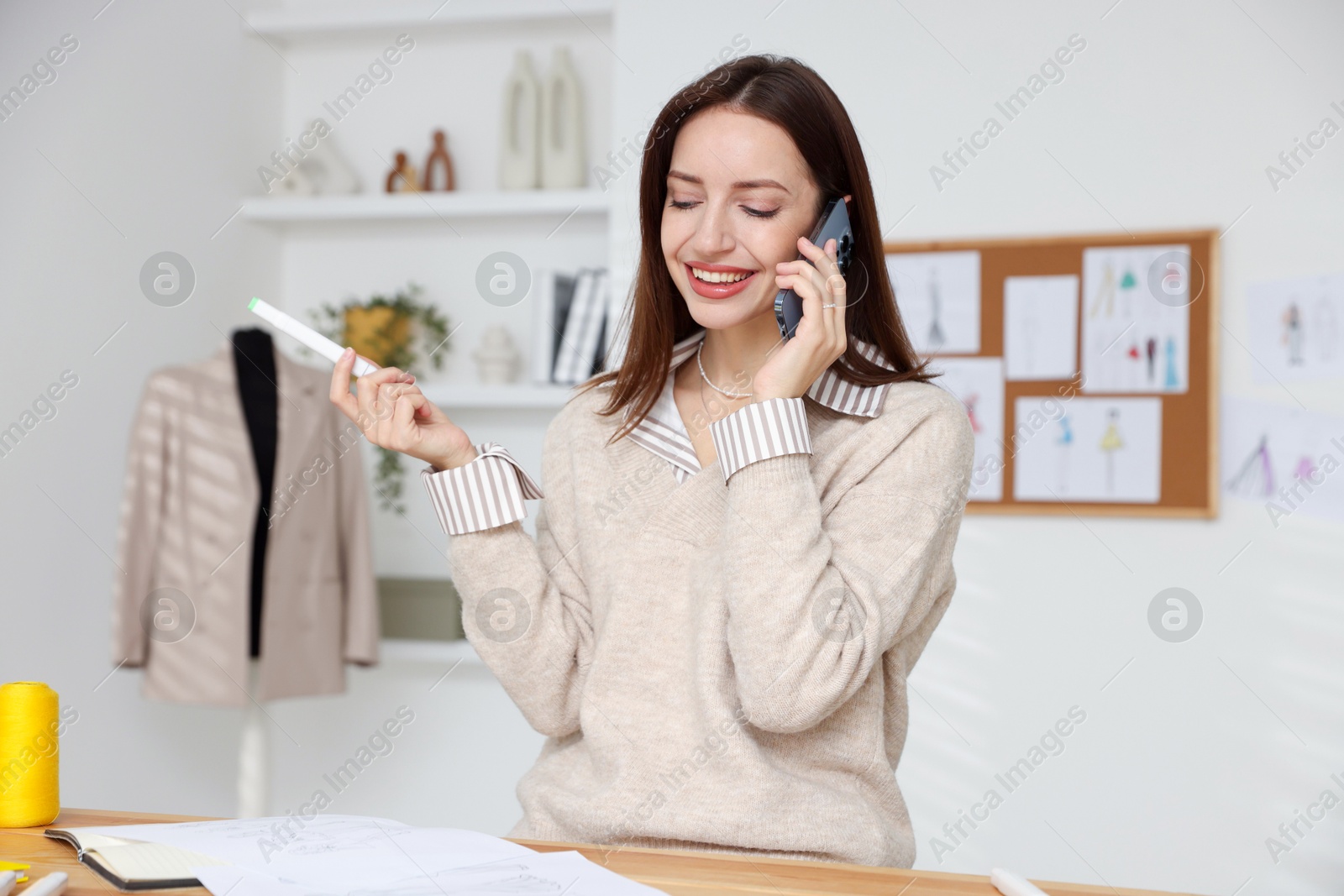 Photo of Fashion designer talking on smartphone at wooden table in workshop