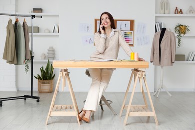 Fashion designer talking on smartphone at wooden table in workshop