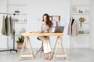 Fashion designer using smartphone at wooden table in workshop