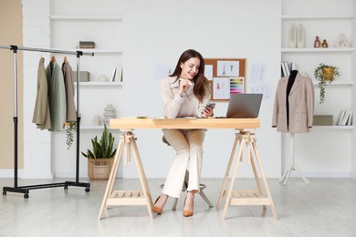 Photo of Fashion designer using smartphone at wooden table in workshop