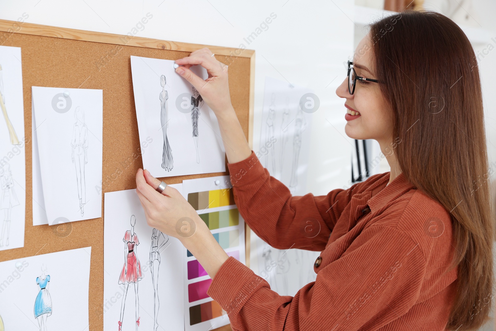 Photo of Fashion designer pinning sketch of clothes to corkboard in workshop