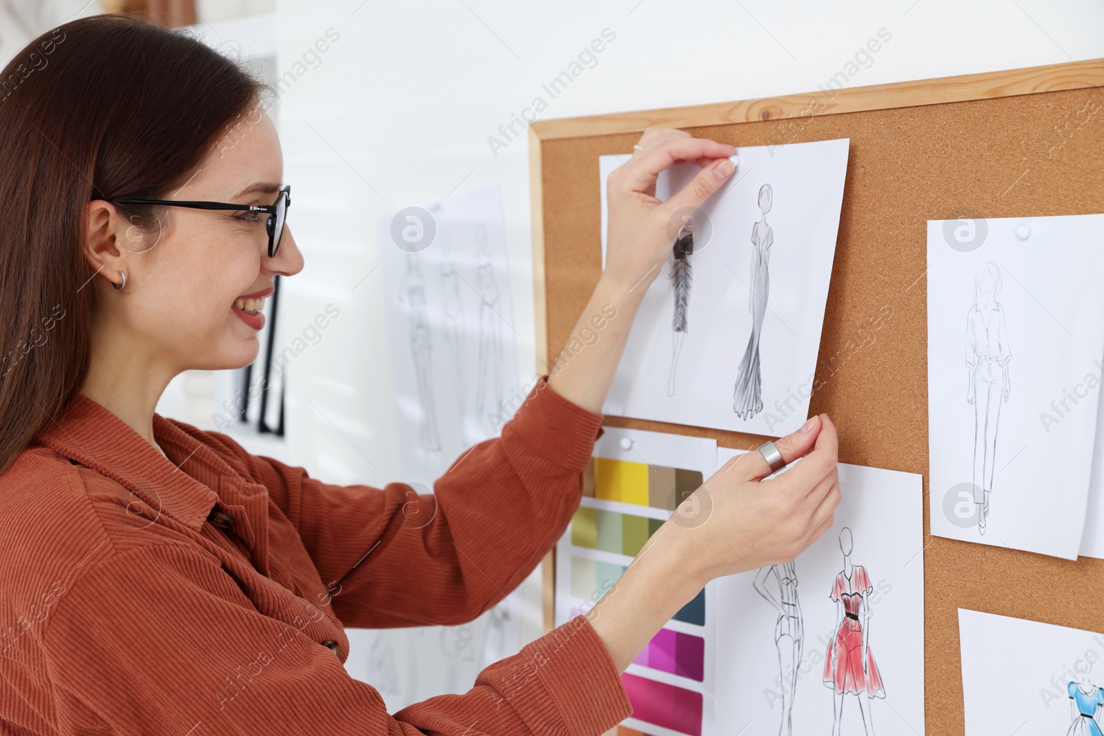 Photo of Fashion designer pinning sketch of clothes to corkboard in workshop